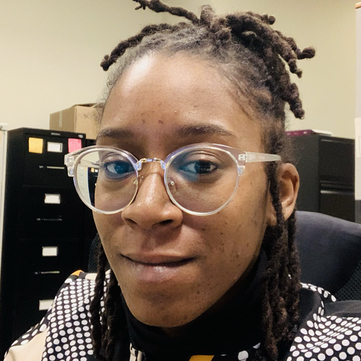 Portrait of Isabel Griffin. A person sitting in an office environment, wearing eyeglasses with clear frames.