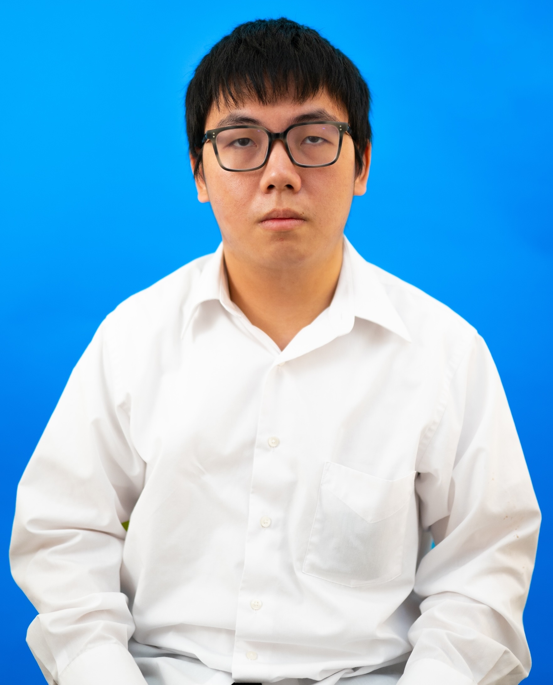 Photo of a man with glasses, wearing a button-down shirt, in front of a blue background.