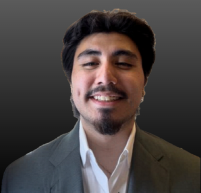 A men in a grey blazer wearing a white button-down shirt in front of a darker grey background.