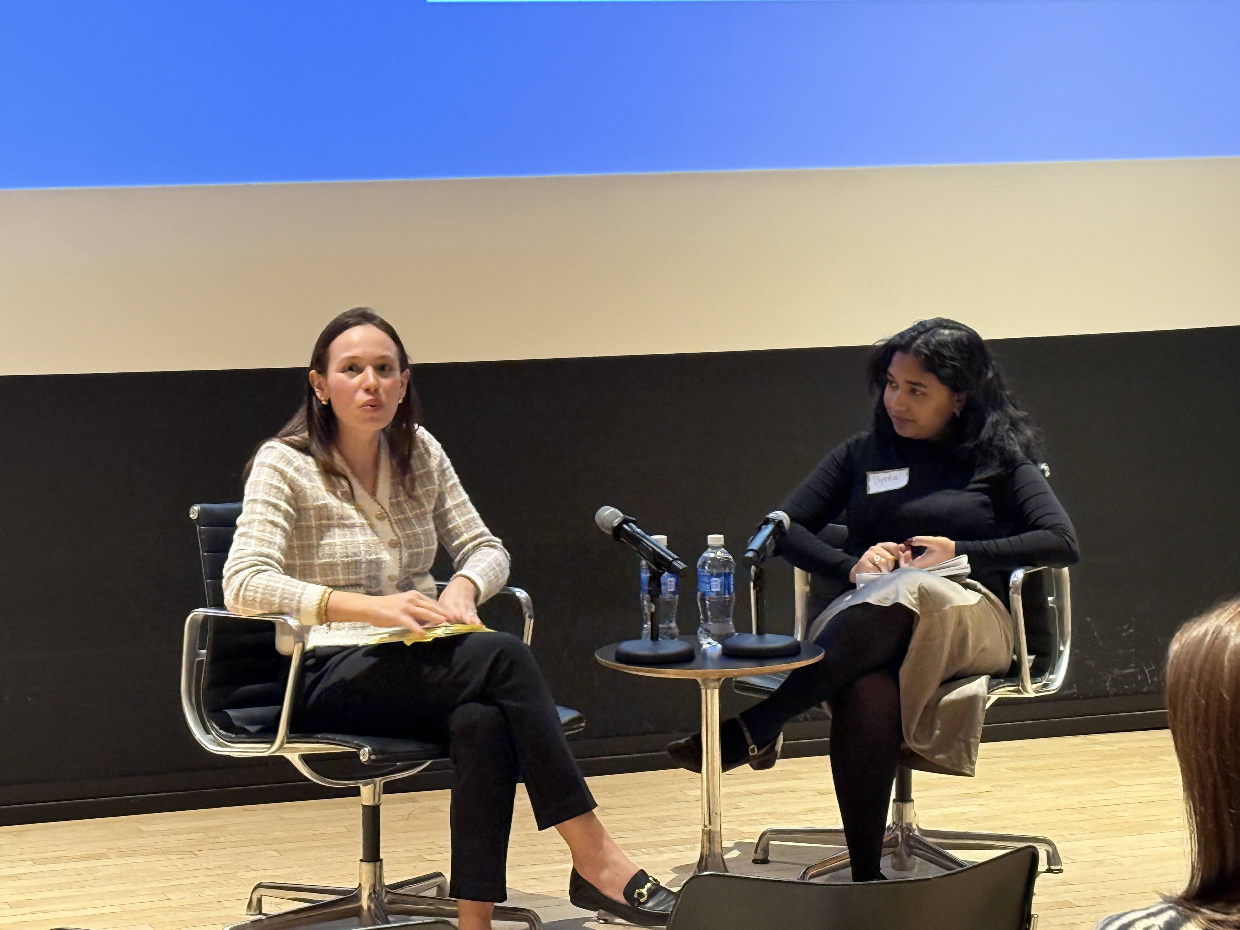 two women sitting on chairs, having a discussion, with a table between them