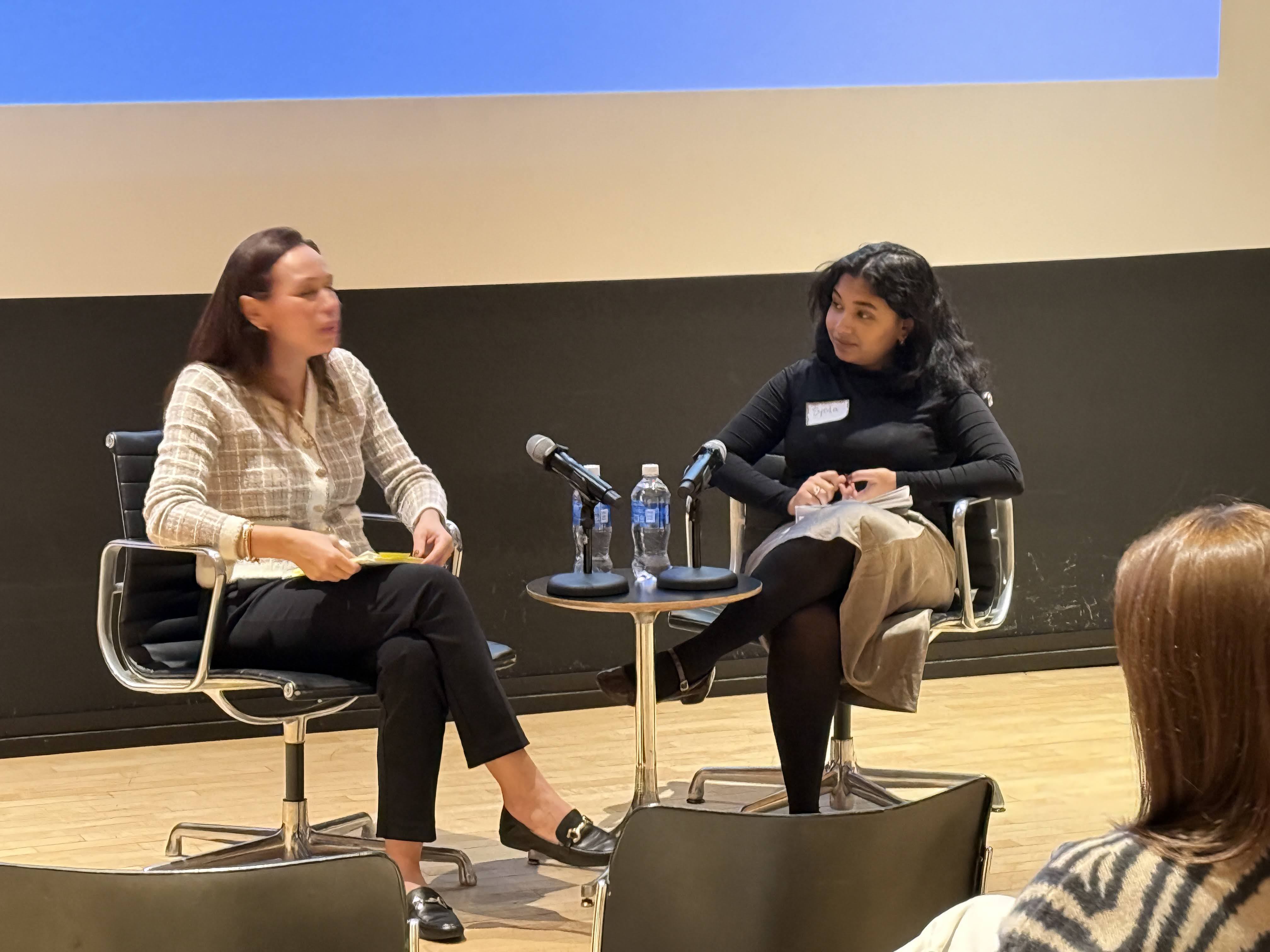 two women sitting on chairs, having a discussion, with a table between them