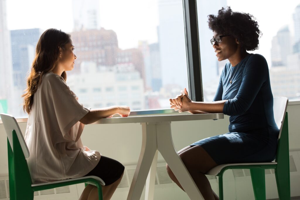 two women sitting opposite each other at a desk, by a window.