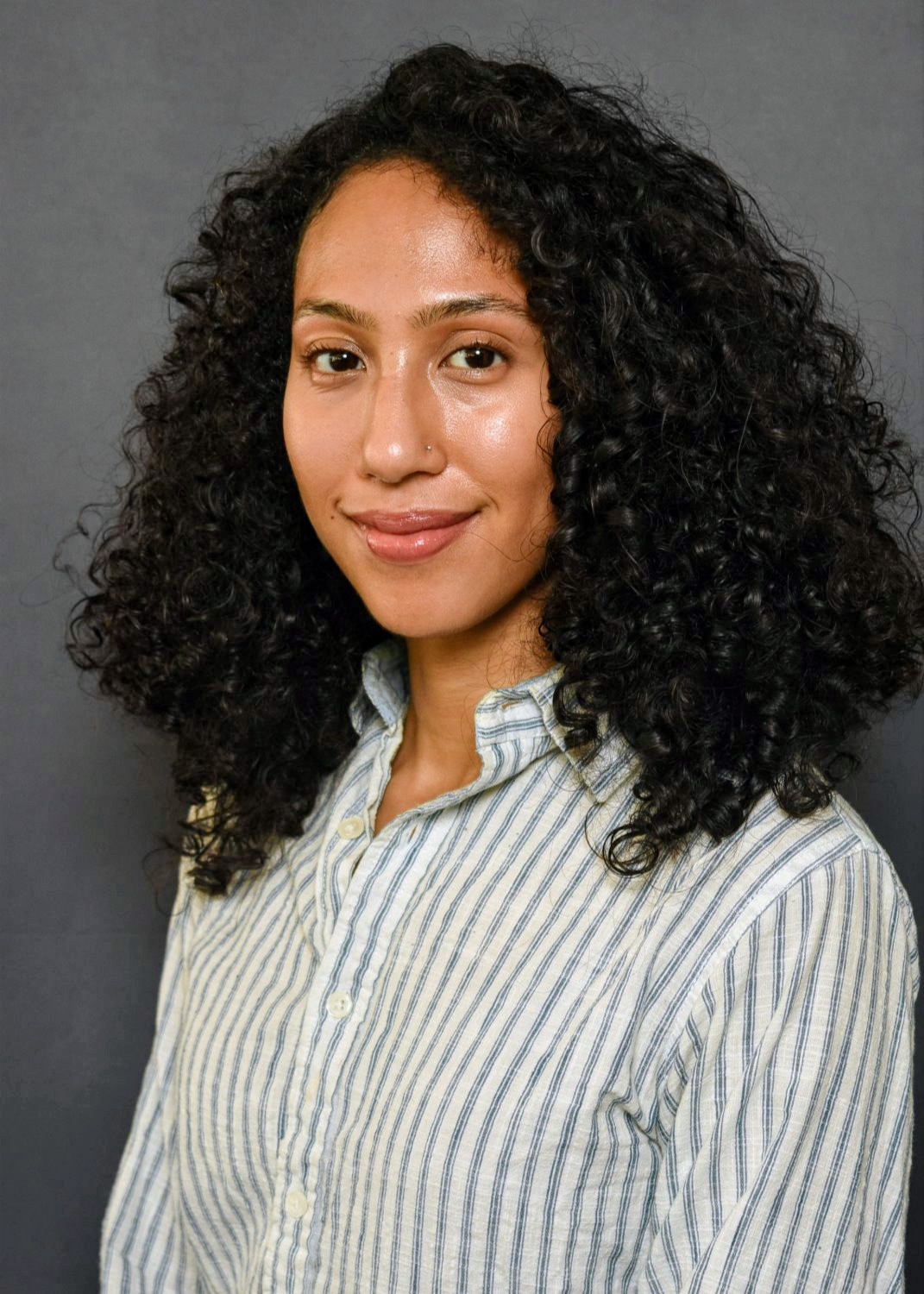 Photo of a woman with a white button down shirt with blue vertical stripes against a grey background.